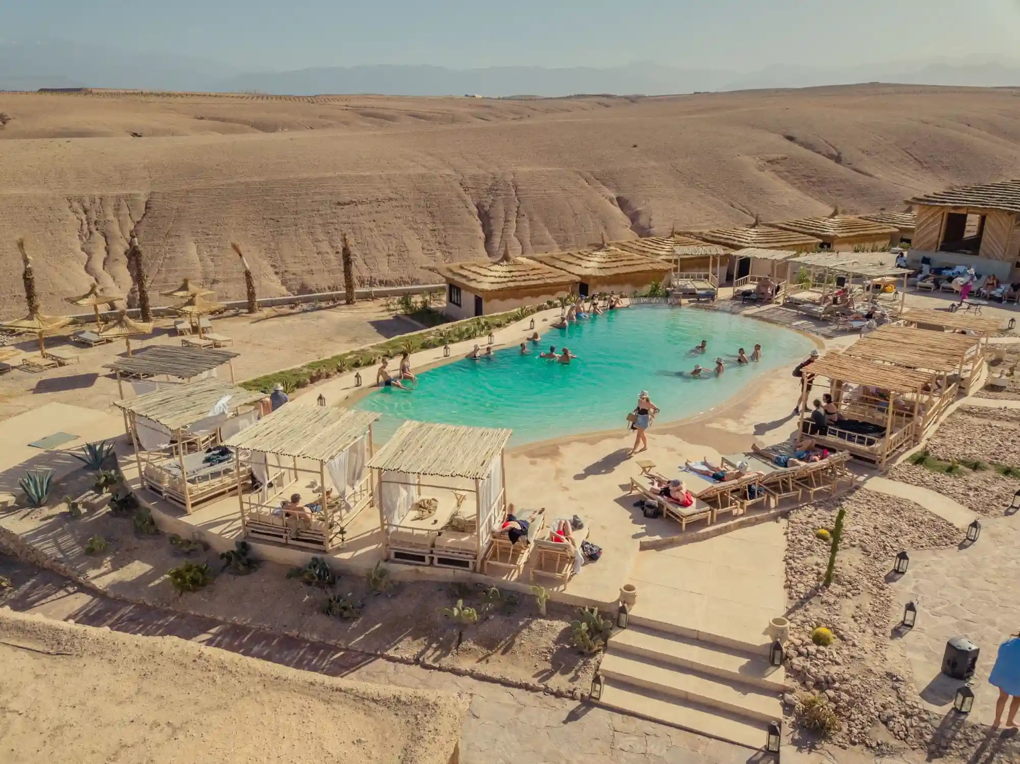 Vue en hauteur de la piscine et des espaces de repos entourés par le désert d’Agafay