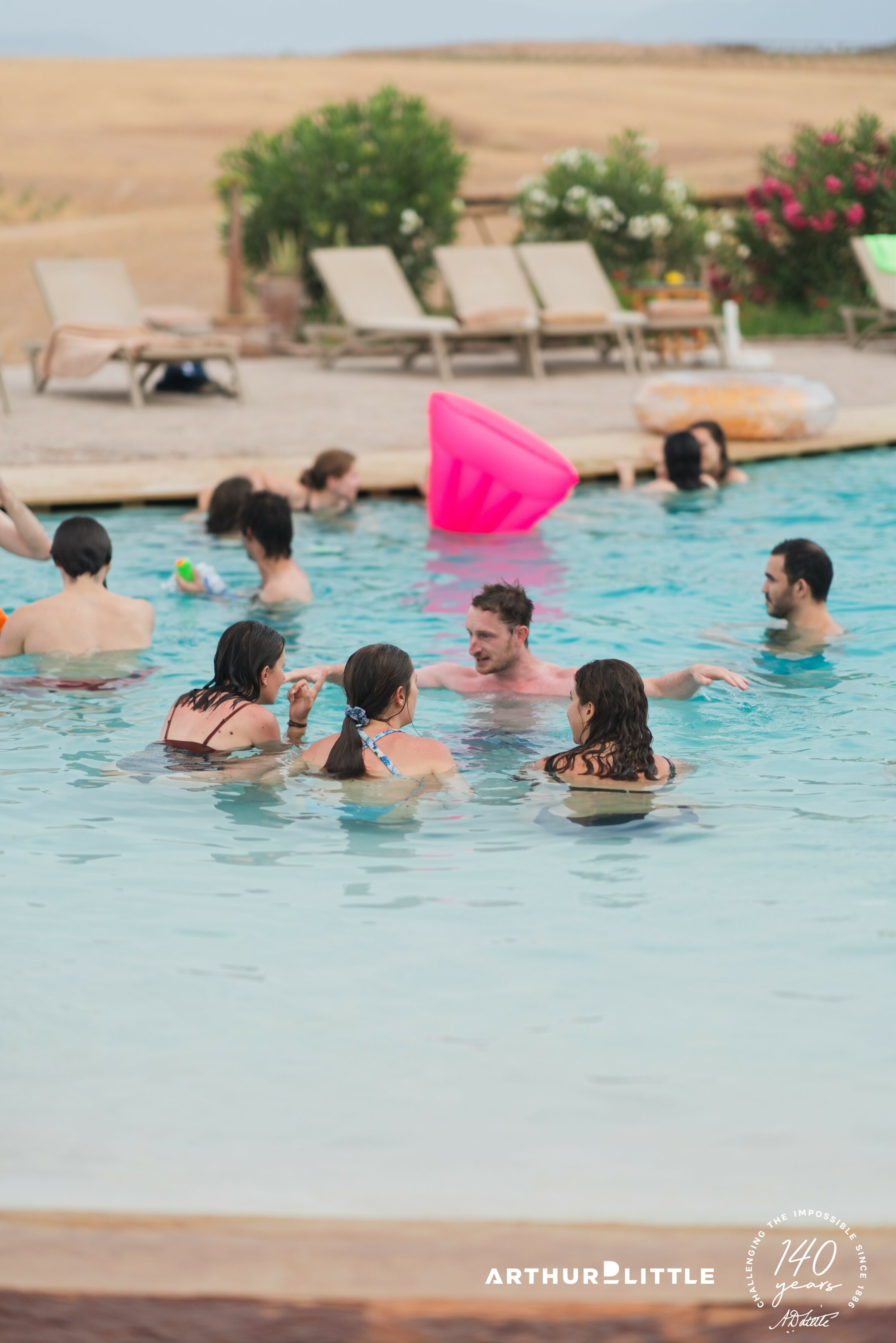 Un groupe de collaborateurs discute dans la piscine avec le désert d’Agafay en arrière-plan